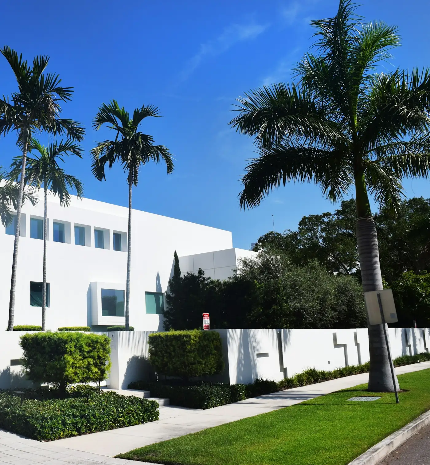 Modern white stucco residence in Sarasota behind a low garden wall and clipped hedges, framed by royal palms under a clear sky