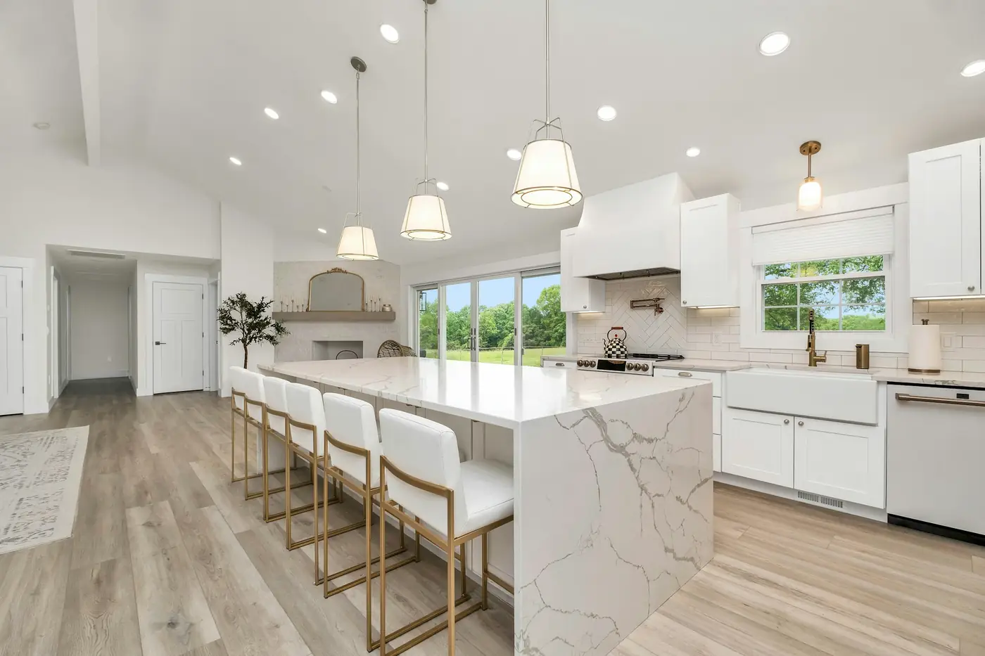 Finished renovated kitchen with white shaker cabinets, a marble waterfall island with four counter stools, pendant lights, and light wood-look flooring