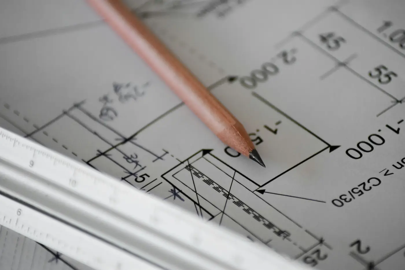 Close-up of a pencil and scale ruler resting on dimensioned construction drawings