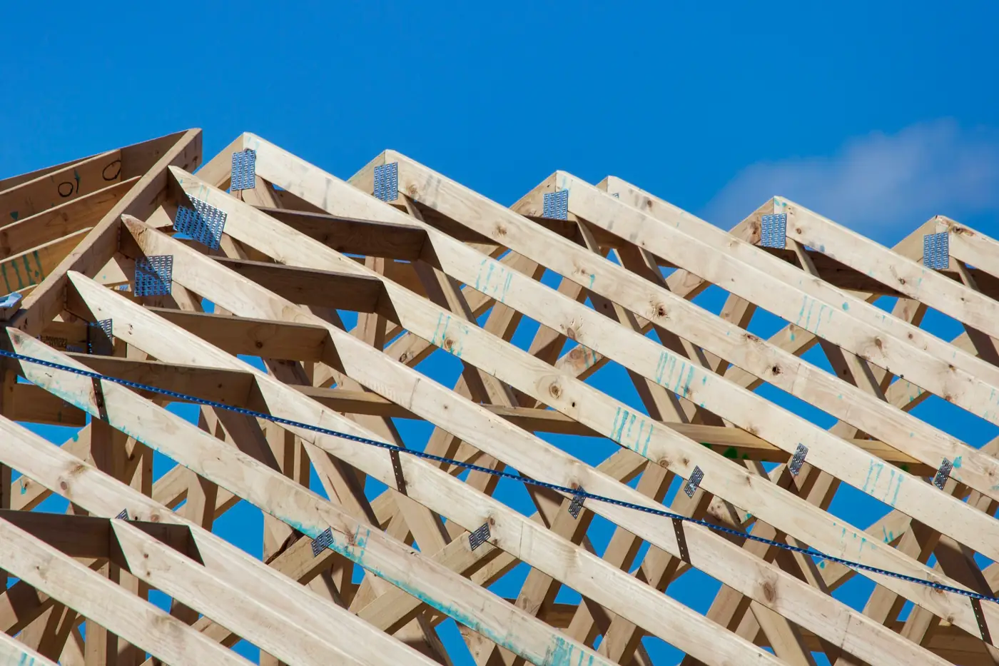Rows of newly set timber roof trusses on a house under construction, seen from below against a deep blue sky