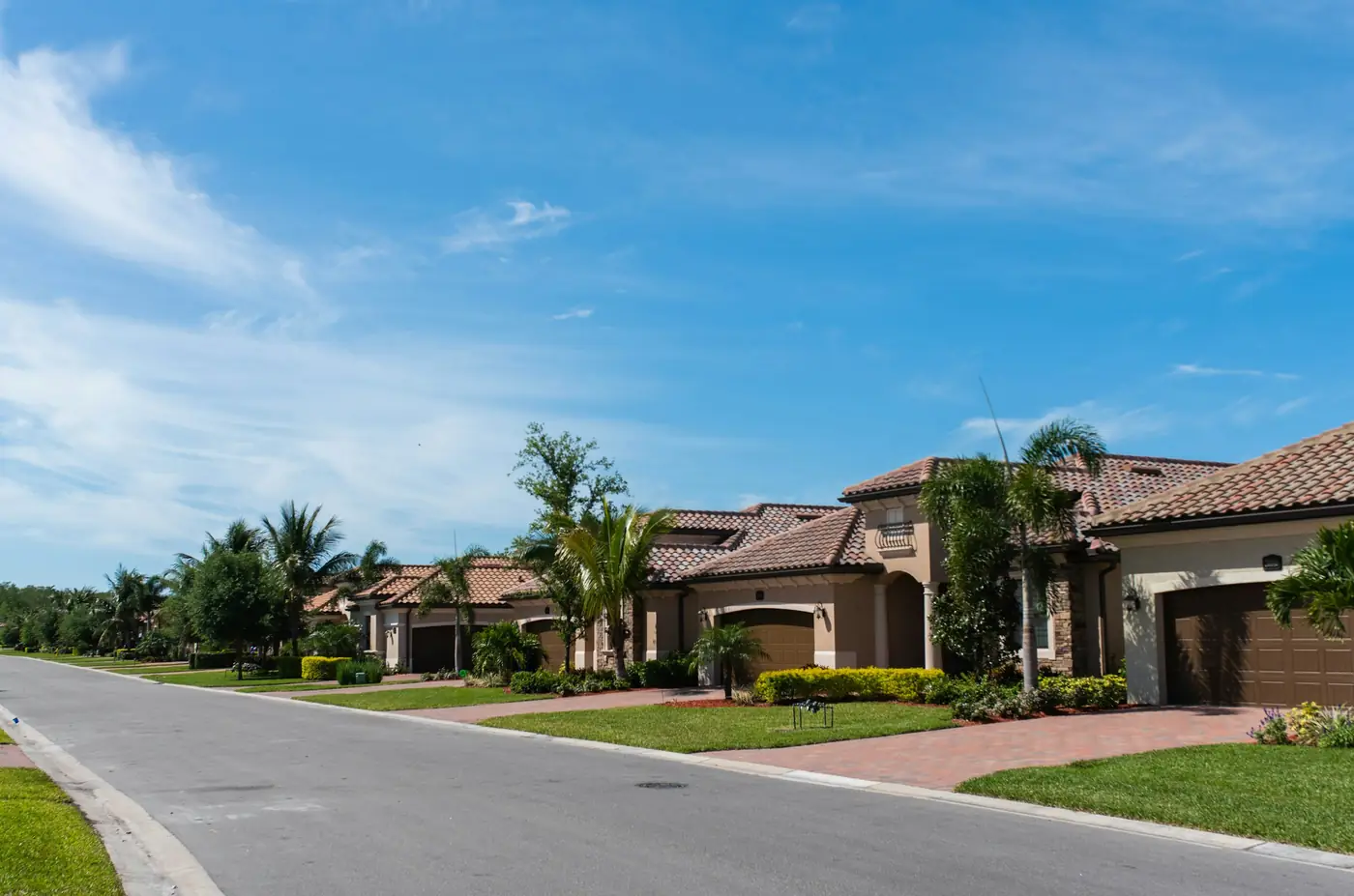 Quiet residential street of stucco, tile-roof homes with palms, paver driveways, and manicured lawns