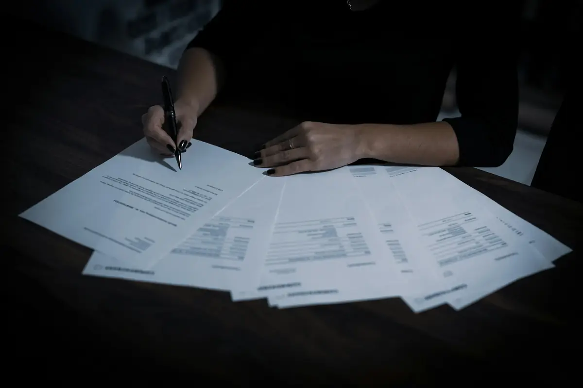 Hands reviewing and signing a fanned stack of loan documents on a dark desk