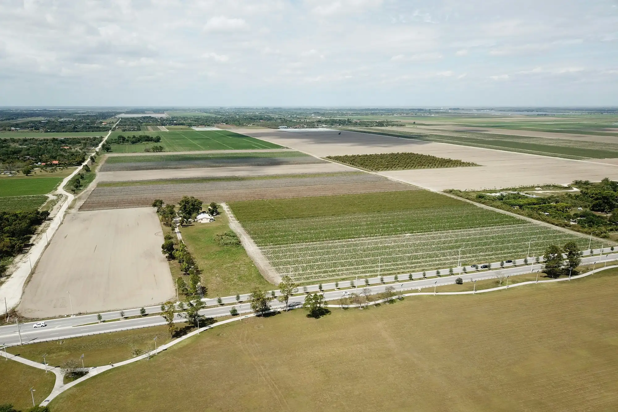 Aerial view of cleared and cultivated parcels on the edge of Miami-Dade County, divided by a two-lane road and stretching flat to the horizon